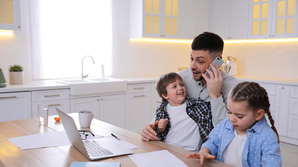 A man speaks on a cell phone with a small child on his lap. Another child stands next to him.