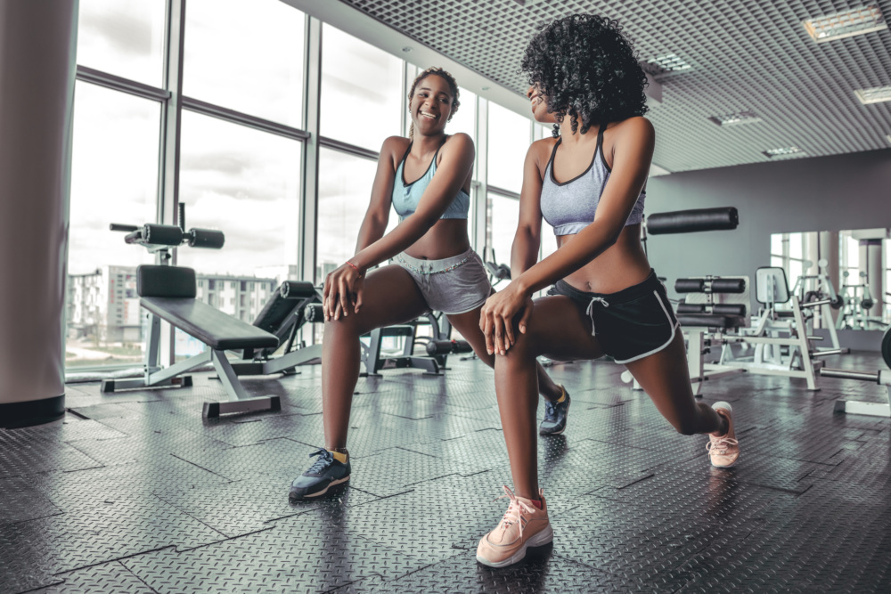 Two young women do a lunge in a gym