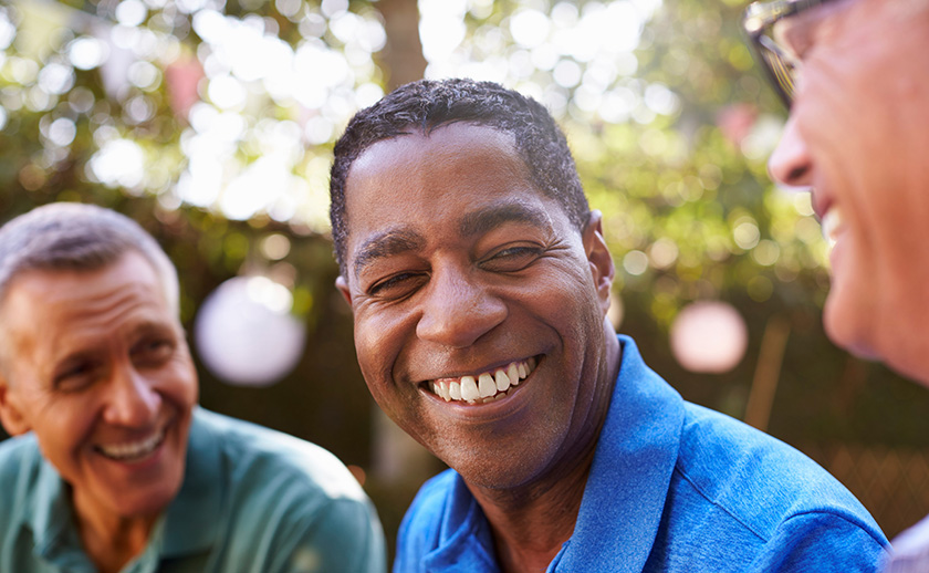 Close up of three men in their 50s chatting to each other outside.