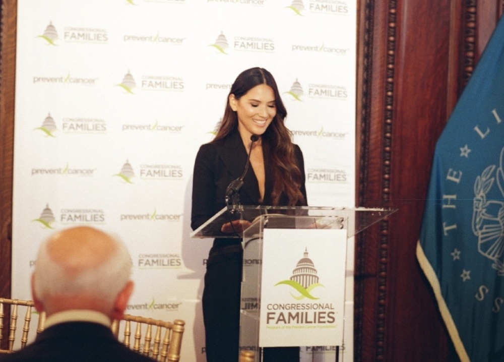 Actress Olivia Munn stands at the podium with her award at the 2025 Congressional Families Luncheon Award ceremony.