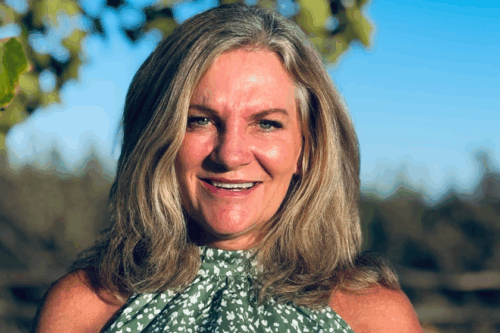 A photo of Jen smiling outside on a sunny day