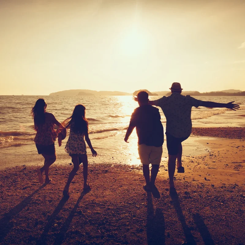 Silhouette of four people running on a beach towards the water at sunset.